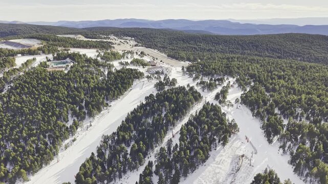 Drone flight parallel to a snowy mountain ski slope surrounded by dense pine forest, winter landscape, alpine terrain, ski resort infrastructure, peaceful nature, scenic aerial motion, winter tourism 