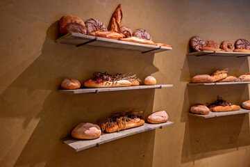 The image displays a stylish, minimalist bakery display featuring various types of artisan bread on three shelves against a warm, textured wal