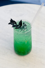 Bright green cocktail with ice and dark garnish in a glass on the table.