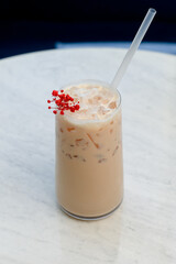 Cold milk coffee drink with ice and red decoration on white table.