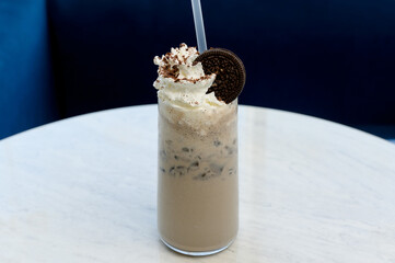 Milk coffee cocktail with ice, whipped cream and cookies on a white table