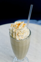 Vanilla milkshake with whipped cream and orange sprinkles in a tall glass