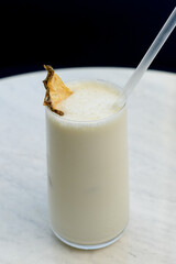 Vanilla milkshake with ice garnished with dried pineapple and a straw
