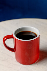 A red ceramic mug with black coffee stands on a white marble table