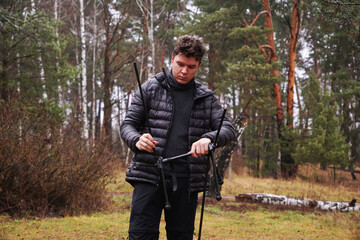 Fototapeta premium A man on a camping trip is busy assembling a chair frame, camping furniture, outdoor recreation, a picnic in the forest, and collecting elements
