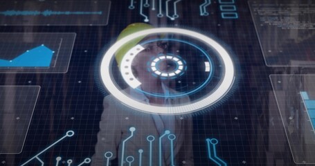 Standing engineer with yellow hard hat and blazer using circular HUD and graphs in control room