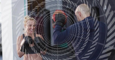 Punching woman in black sports bra throwing punches in gym, coach holding pads, copy space