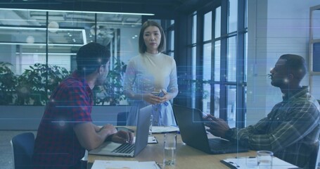 Presenting team lead in light blouse and skirt addressing team at meeting table with two laptops