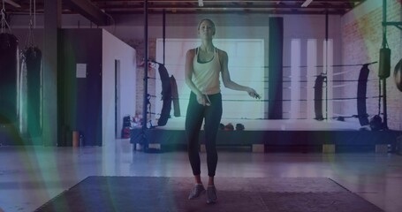Skipping woman in sportswear jumping rope on rubber mat in boxing gym, with ring