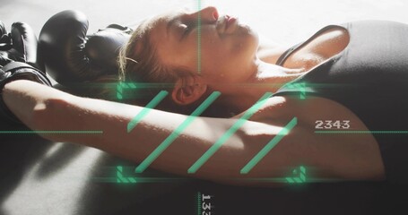 Lying female athlete resting on padded mat at gym, black top, gloves, green HUD numeric readouts