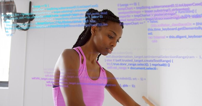 Stretching braided woman wearing pink tank top in studio, holding ballet barre with digital code - Powered by Adobe