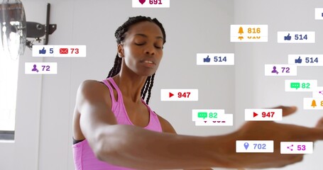 Stretching woman in pink tank extending arms in white studio, with floating social icons, wall fan