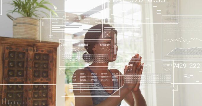 Praying woman wearing gray tank at home near window, with over-ear headphones and UI overlays
