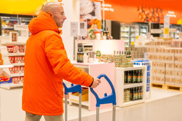 young man in orange jacket pushing warehouse trolley, male customer in self service furniture store, selecting home goods accessories, retail interior design planning, warehouse aisle background