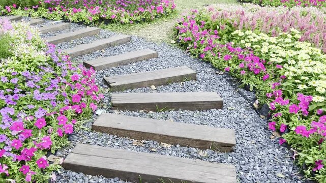 A wooden sleeper and gravel path winding through a colorful flower garden.