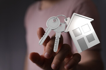 A person's hand holding keys with a house-shaped keychain, symbolizing homeownership, property, and new beginnings. Represents real estate and i