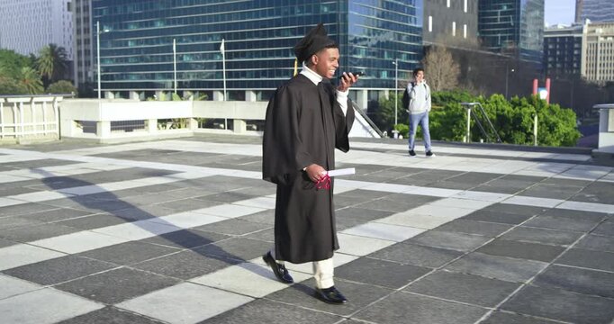 Graduating African American man in cap  and  gown walking on rooftop calling home taking diploma sel