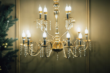 Elegant close-up of a glowing golden chandelier with crystal details, creating a luxurious, warm, and festive atmosphere in an ornate interior space.