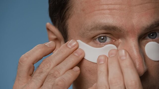 Close up of Caucasian man looking at himself and applying cold hydrogel patch under eye after cleansing