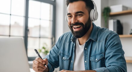 Engaged Focus: A man with a beard immersed in his work, attentively listening through headphones while making notes on a notepad. Capturing focus, learning, technology and productivity.