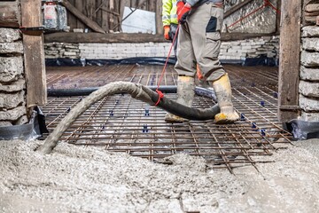 An indoor construction site displays the pouring of a concrete slab with reinforcement mesh,...