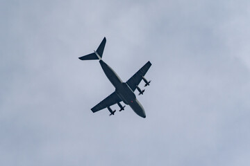Four-engine turboprop aircraft banks across the sky in a dramatic underside view. Dark silhouette and spinning propellers cut through high clouds.
