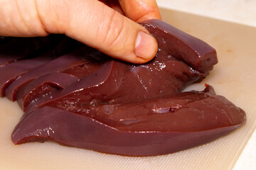 Hand Holding and Bending a Piece of Fresh, Raw Liver on a Textured Cutting Board