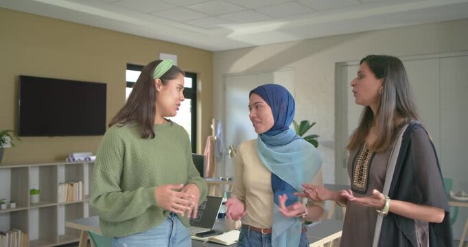 Walking into office sparking desk discussion among diverse female coworkers and smiling at camera
