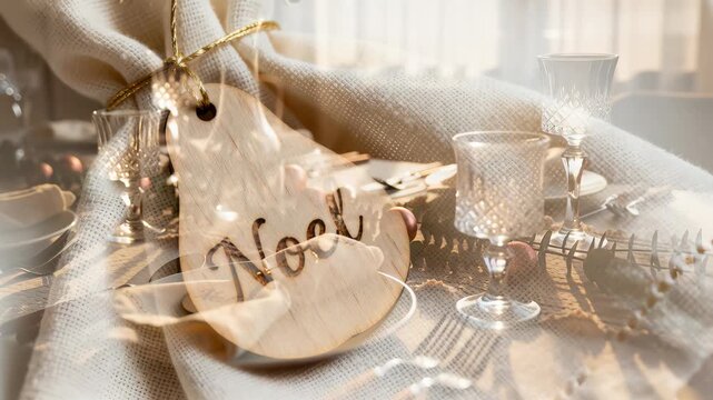 Wooden tag engraved with Noel attached to a tied cloth napkin on neutral textured fabric. There is an empty fabric area providing copyspace for a holiday message or branding and subtle tabletop detail