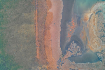 Aerial top down view of orange chemical runoff pollution near green field. Industrial waste sludge texture and environmental danger background.