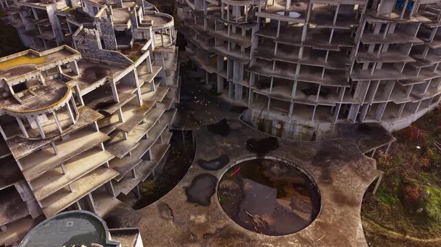 Amidst overgrown vegetation, the skeletal structures of a forsaken resort rise, revealing crumbling concrete and scattered debris reflecting years of neglect and decay.