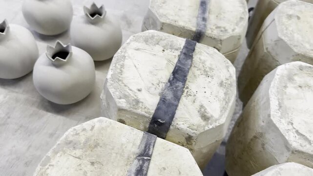 Studio Workflow: Collection of smooth, handmade wheel-thrown clay vessels Greenware next to slip-casting plaster molds used for creating identical decorative pomegranate ceramic sculptures.