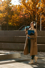 Naklejka premium Woman Walking with Headphones and Coffee in Autumn City