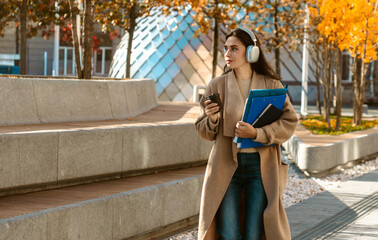 Naklejka premium Woman Walking with Headphones and Coffee in Autumn City