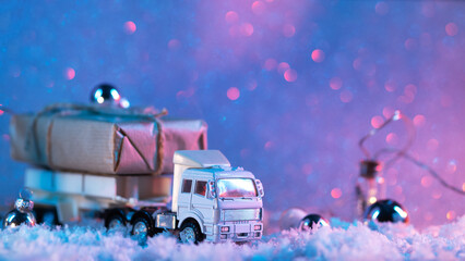 A toy truck is transporting a gift box, a Christmas and New Year's snow colored background with copy space.