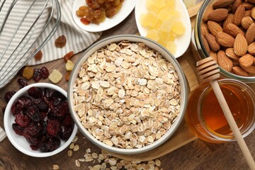 Making granola. Oat flakes in bowl, dried fruits, almond nuts and honey on wooden table, flat lay