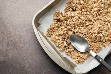 Making granola. Oat flakes with dried fruits and spoon in tray on grey table, top view. Space for text