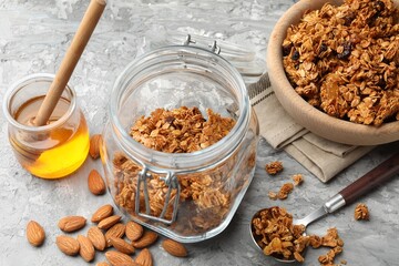 Tasty granola in glass jar and ingredients on light grey table, closeup