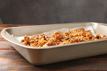 Tasty granola in tray and ingredients on wooden table, closeup