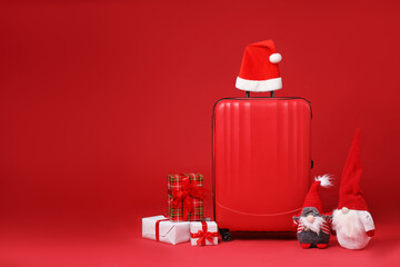 Christmas vacation. Stylish suitcase, Santa hat, gift boxes and decorative gnomes on red...