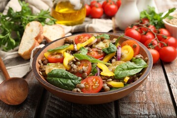 Tasty lentil salad, ingredients and bread on wooden table, closeup