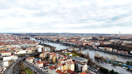 Obraz premium Wide panoramic view of a dense urban area divided by a winding river. Mixed architecture, residential rooftops, bridges, and waterways under cloudy sky, illustrating city life and spatial structure. 