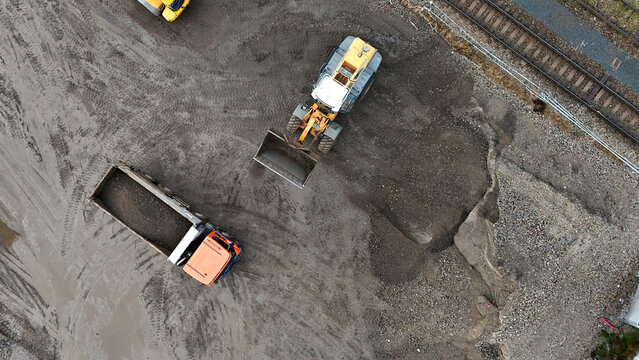 Top-down aerial view of an active construction site with excavator and truck near an excavation pit. Industrial textures, infrastructure work, precise machinery operation, and development progress.

