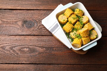 Pieces of boiled corncobs with green onion in baking dish on wooden table, top view. Space for text
