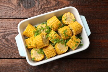 Pieces of boiled corncobs with green onion in baking dish on wooden table, top view