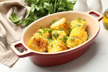 Pieces of grilled corn cobs with green onions on white table, closeup