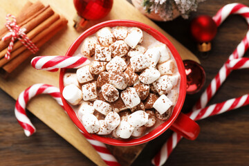 Tasty cocoa with marshmallows, candy canes, cinnamon and Christmas decor on wooden table, flat lay
