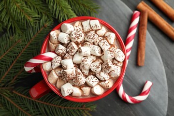 Tasty cocoa with marshmallows, candy canes, cinnamon and Christmas decor on black table, flat lay