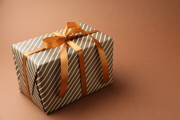 Beautiful wrapped gift on brown background, closeup. Space for text