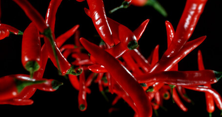 Flying red chili peppers captured in motion against a dark background. Vibrant colors, spicy food concept, and dynamic composition ideal for culinary, advertising, and creative projects.